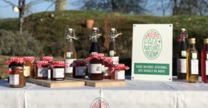 Des bocaux de conserves et des bouteilles de jus de fruits issus de produits locaux sont exposés sur une table à côté d'un panneau indiquant le Parc Naturel Régional des Vosges du Nord.